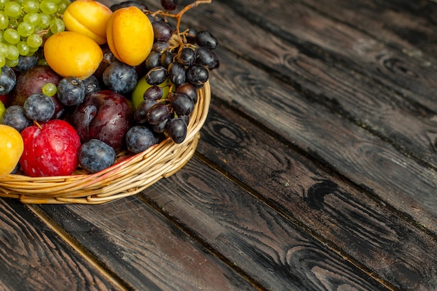 Vue avant du panier avec des fruits fruits doux et aigres tels que les raisins abricots prunes sur le fond rustique brun