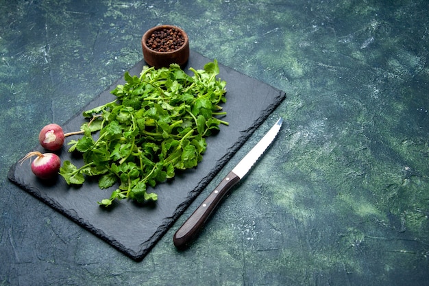 Vue avant du paquet de coriandre poivre de radis frais sur une planche à découper en bois et un couteau sur le côté droit sur fond de couleurs mélangées noir vert avec espace libre