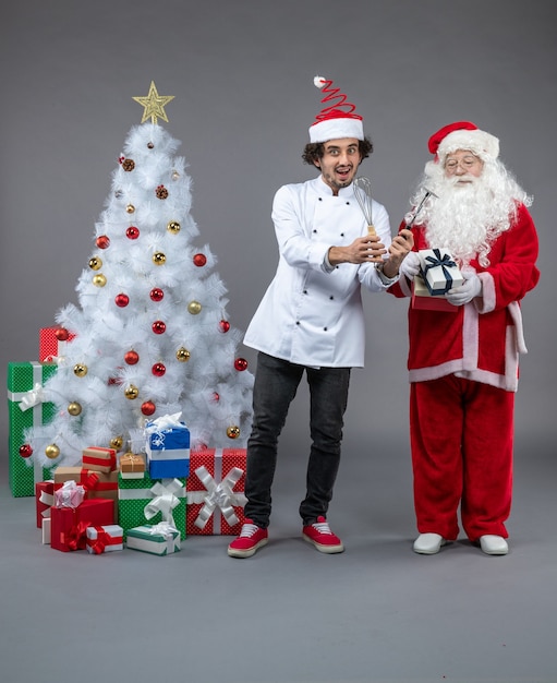 Vue Avant Du Père Noël Avec Cuisinier Masculin Autour De Cadeaux De Noël Sur Mur Gris