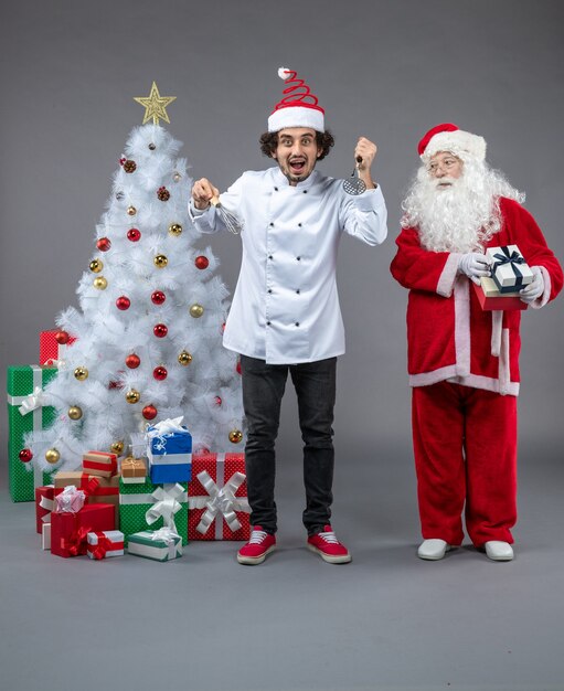 Vue avant du père Noël avec cuisinier masculin autour de cadeaux de Noël sur mur gris