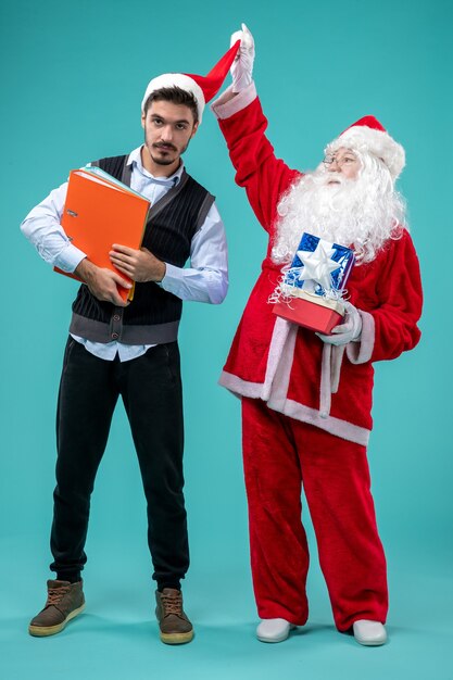 Photo gratuite vue avant du père noël avec jeune homme et présente sur un bureau bleu