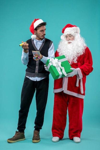 Photo gratuite vue avant du père noël avec jeune homme qui prend des notes sur le fond bleu