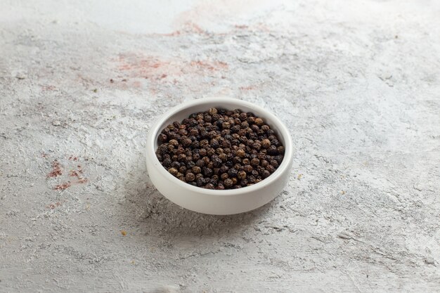 Vue avant du poivre noir peu à l'intérieur du pot blanc sur une surface blanche