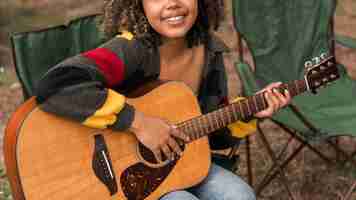 Photo gratuite vue avant du smiley femme jouant de la guitare en camping en plein air