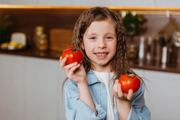 Vue avant du smiley petite fille dans la cuisine avec des tomates