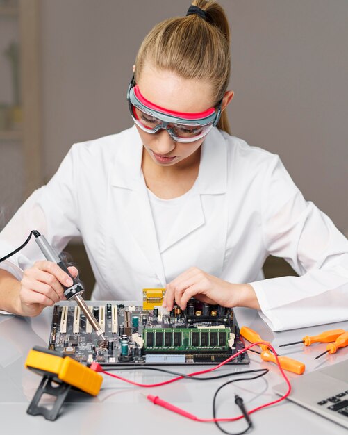 Vue avant du technicien féminin avec fer à souder et carte électronique