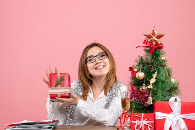 Vue avant du travailleur féminin assis autour de cadeaux de Noël et arbre sur rose