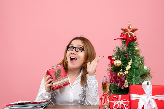 Vue avant du travailleur féminin assis autour de cadeaux de Noël et arbre sur rose