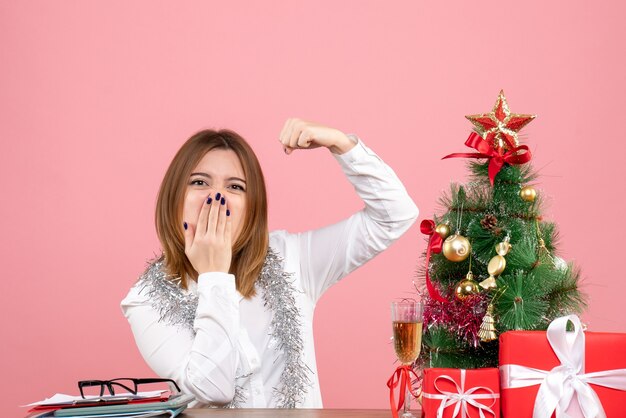 Vue avant du travailleur féminin assis derrière sa table avec des cadeaux de Noël sur rose