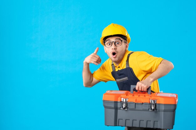 Vue avant du travailleur masculin en uniforme jaune avec boîte à outils sur la surface bleue