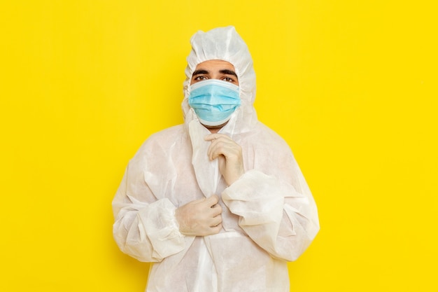 Vue avant du travailleur scientifique masculin en tenue de protection spéciale portant son masque sur mur jaune