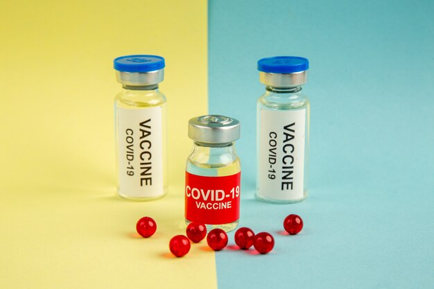 Vue avant du vaccin contre le coronavirus avec des pilules rouges sur fond jaune-bleu virus de l'hôpital laboratoire de couleur pandémique covid- science drogue