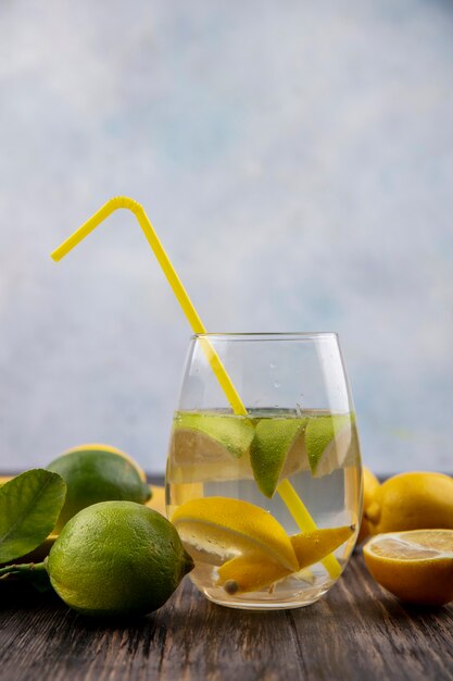 Vue avant du verre d'eau avec des tranches de citron avec de la chaux et de la paille jaune