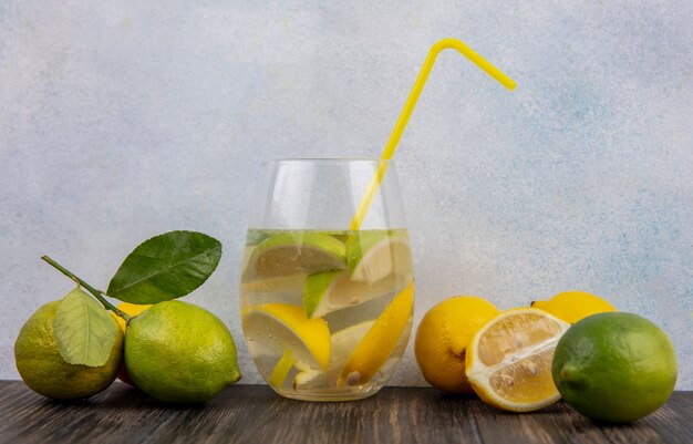 Vue avant du verre d'eau avec des tranches de citron avec de la chaux et de la paille jaune