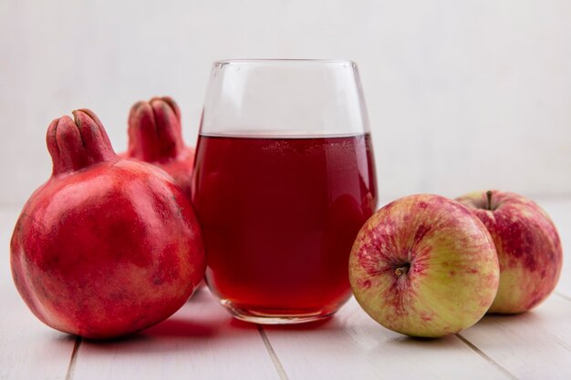 Vue avant du verre de jus de grenade avec pommes et grenades sur mur blanc