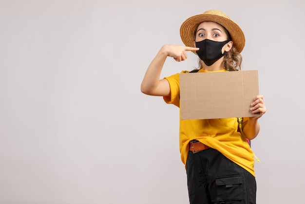 Vue avant du voyageur féminin avec sac à dos tenant le doigt pointé en carton son masque sur mur gris