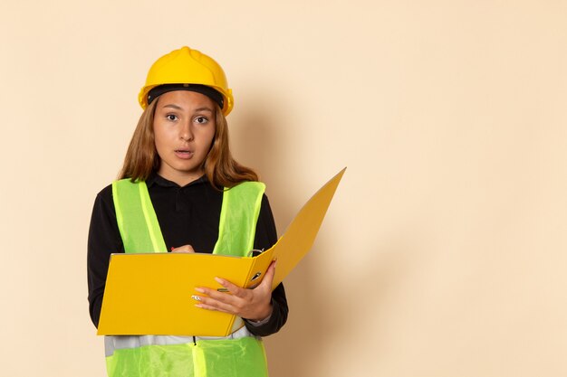 Vue avant femme constructeur en casque jaune tenant le fichier jaune écrit des notes sur le mur blanc