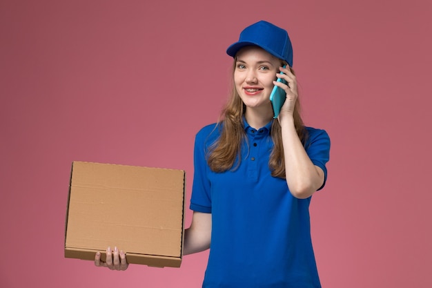 Vue avant femme courrier en uniforme bleu tenant la boîte de livraison de nourriture et parler au téléphone sur le travail de l'entreprise uniforme de bureau rose