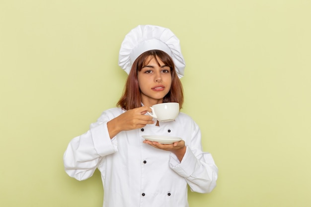 Vue avant femme cuisinier en costume de cuisinier blanc, boire du thé sur une surface verte