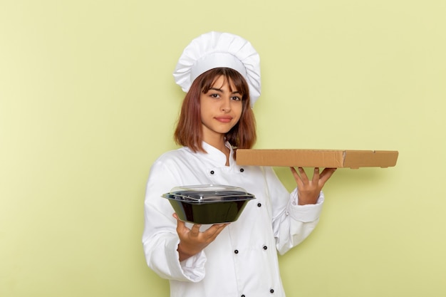 Vue Avant Femme Cuisinier En Costume De Cuisinier Blanc Tenant La Boîte De Nourriture Et Bol Noir Sur La Surface Verte