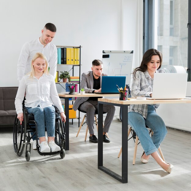 Vue avant d'une femme en fauteuil roulant aidée par un collègue au bureau