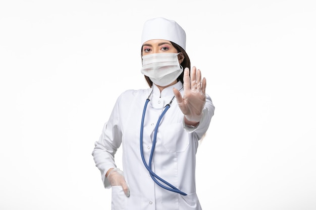 Vue avant femme médecin en costume médical stérile blanc avec masque en raison de covid- sur la maladie de bureau blanc covid- maladie à virus pandémique