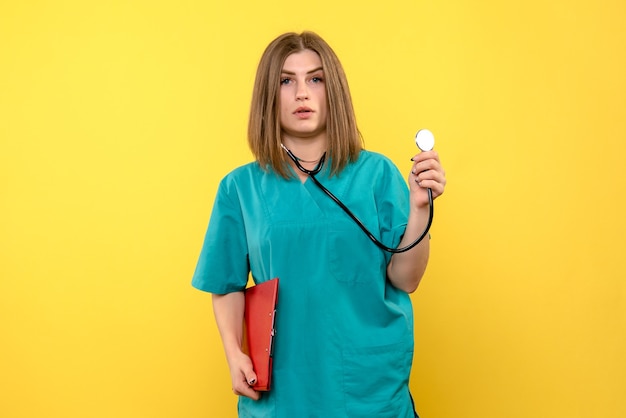 Vue avant de la femme médecin avec tonomètre et fichiers sur mur jaune