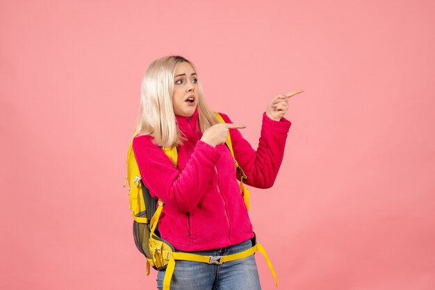 Vue avant femme voyageur dans des vêtements décontractés portant un sac à dos pointant vers la droite