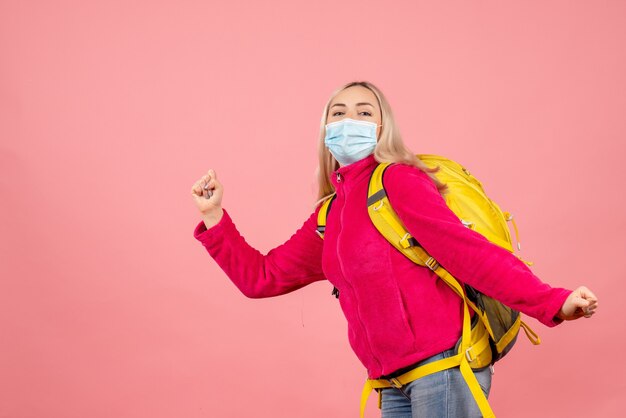 Vue avant femme voyageur avec sac à dos jaune portant un masque en cours d'exécution