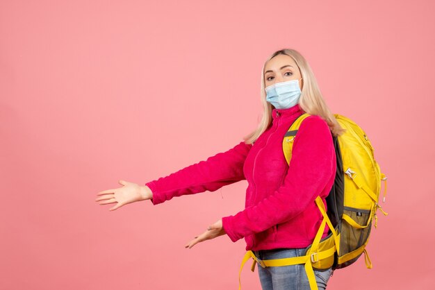 Vue avant femme voyageur avec sac à dos jaune portant un masque montrant quelque chose