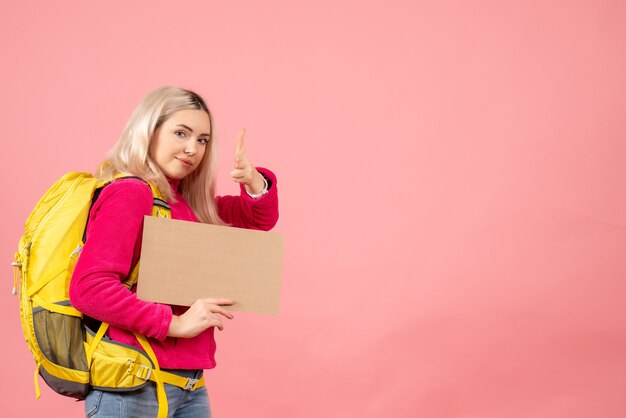 Vue avant femme voyageur avec sac à dos mettant le pistolet à doigt à la caméra tenant le carton