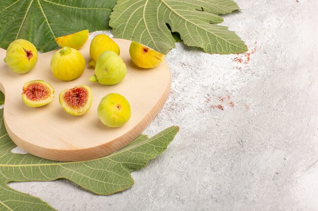 Vue avant des fœtus sucrés de figues fraîches avec des feuilles sur un bureau blanc