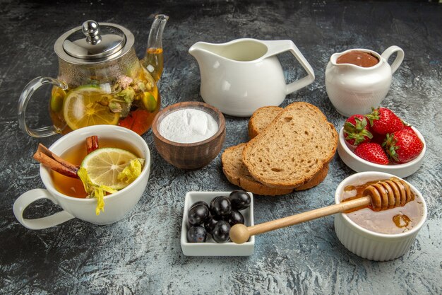 Vue avant des fraises fraîches avec du pain au thé et du miel sur la surface sombre des aliments sucrés de fruits