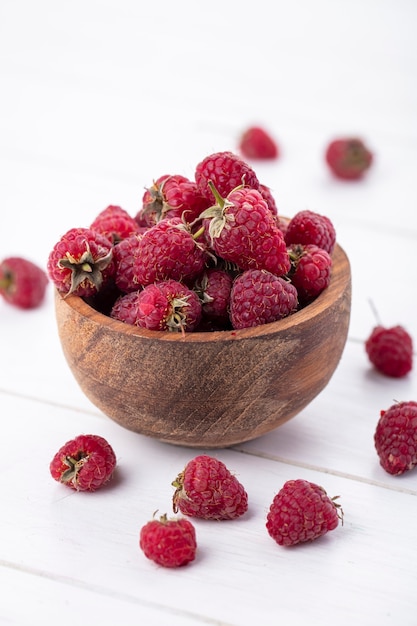 Vue avant de framboises dans un bol en bois sur une surface blanche