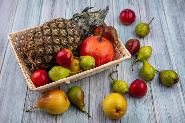 Vue avant des fruits comme ananas grenade pêche prune dans le panier et sur la surface en bois