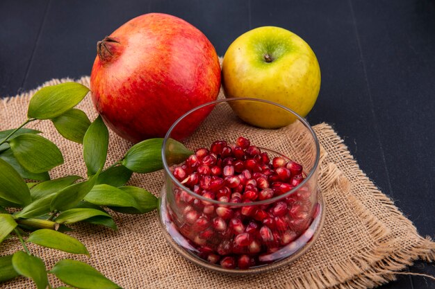 Vue avant des fruits comme les baies de grenade dans un bol avec pomme entière et grenade avec des feuilles sur un sac sur une surface noire