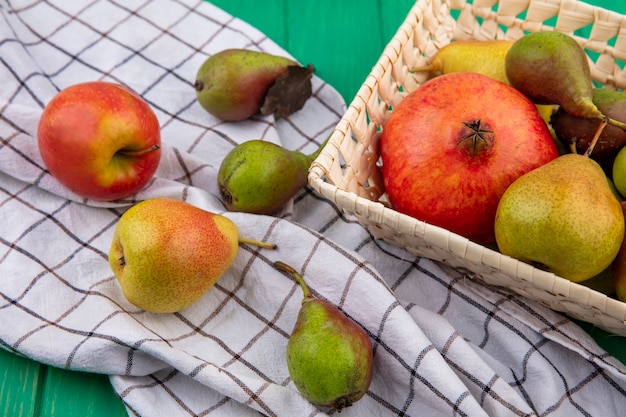 Vue avant des fruits comme la grenade et la pêche dans le panier et sur un tissu à carreaux sur une surface verte