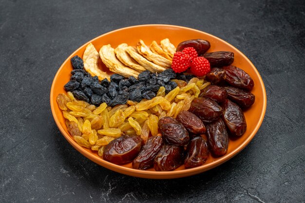 Vue avant des fruits secs avec des raisins secs à l'intérieur de la plaque sur l'espace gris