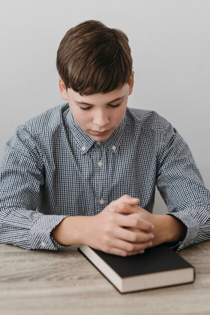 Vue avant garçon priant avec ses mains sur un livre saint