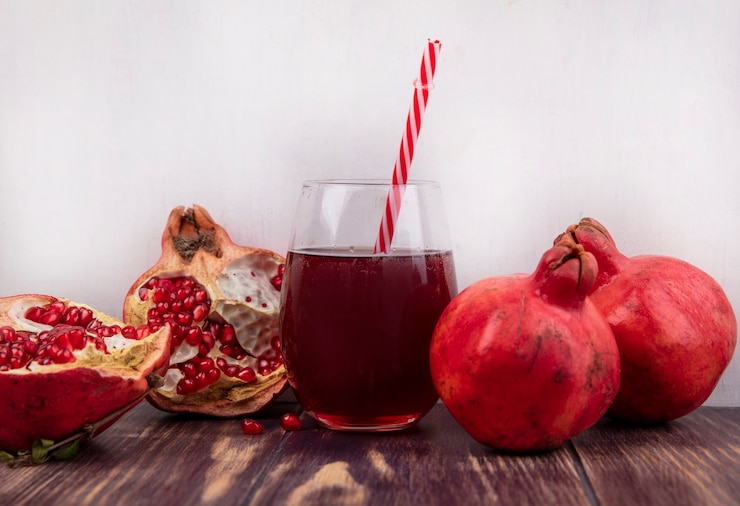 Photo gratuit vue avant des grenades avec un verre de jus et une paille rouge sur un mur en bois