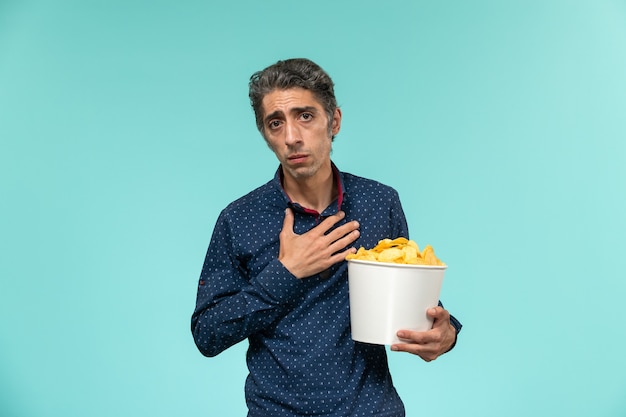 Vue avant, homme d'âge moyen, manger des cips sur un bureau bleu