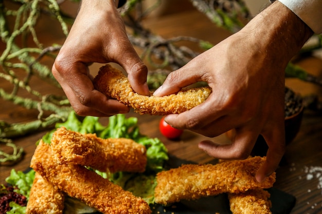 Photo gratuite vue avant l'homme casse les pépites de poulet avec des sauces sur un support