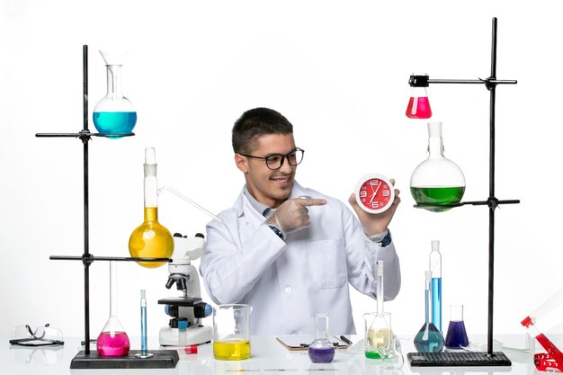 Vue avant de l'homme chimiste en costume médical blanc tenant des horloges sur fond blanc clair de laboratoire scientifique de la maladie du virus Covid