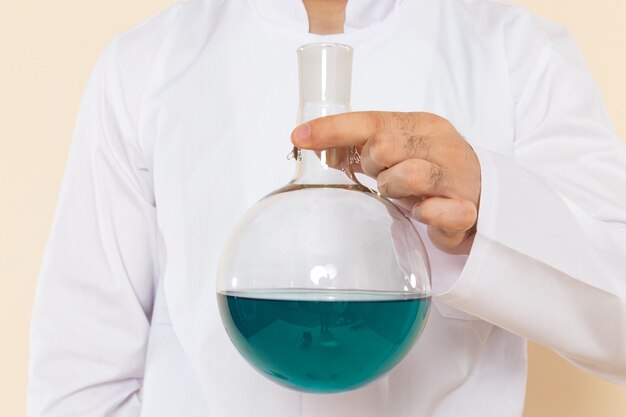 Vue avant de l'homme chimiste en costume spécial blanc tenant le flacon avec une solution bleue sur le bureau de la crème science laboratoire expérience chimie scientifique