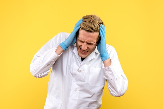 Vue avant de l'homme médecin ayant des maux de tête sur fond jaune covid- human émotion medic