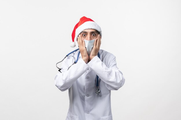 Vue avant de l'homme médecin avec bonnet rouge et masque sur mur blanc nouvelle année pandémie de covid