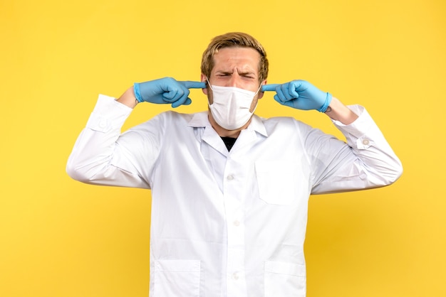 Photo gratuite vue avant de l'homme médecin collant ses oreilles sur fond jaune pandémie covid health medic