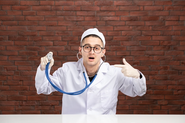 Vue avant de l'homme médecin en costume médical blanc derrière le bureau