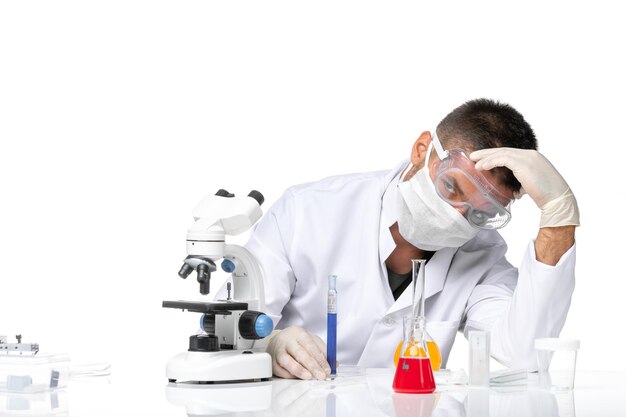 Vue avant de l'homme médecin en costume médical blanc avec masque en raison du travail de covid et a souligné sur l'espace blanc