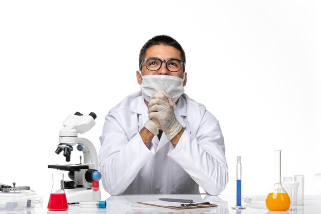 Vue avant de l'homme médecin en costume médical blanc et avec masque rêvant profondément sur un bureau blanc